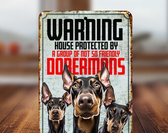 May include: Warning sign with the text "Warning House Protected by a Group of Not So Friendly Dobermans" in red and black lettering. Three Doberman Pinscher dogs are pictured on the sign.