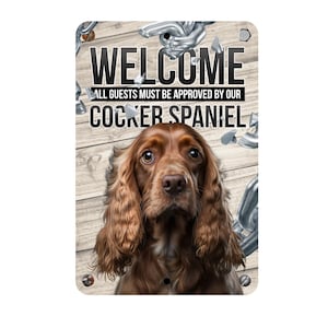 Könnte beinhalten: Willkommensschild mit einem braunen Cocker Spaniel auf einem Holzmaserungshintergrund. Das Schild lautet "Willkommen, Alle Gäste müssen von unserem Cocker Spaniel genehmigt werden."
