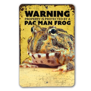 May include: A yellow warning sign with distressed paint and a Pac-Man frog. The sign reads "Warning Property is protected by a Pac-Man Frog".