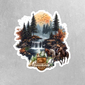 May include: A sticker featuring a scenic landscape with a waterfall, trees, and a sunset. Two people are riding horses in the foreground. The sticker has the text "Dogwood Canyon Nature Park" in a brown shield.