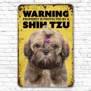 May include: Yellow warning sign with black text that reads "Warning Property is protected by a Shih Tzu". A brown and white Shih Tzu dog with a pink bow is pictured on the sign.