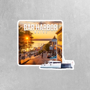 May include: A sticker featuring a scenic sunset view of Bar Harbor, Maine. The sticker shows a street lined with buildings and trees, with a body of water in the background. The text "BAR HARBOR MAINE" is printed in white on a black background at the top of the sticker.