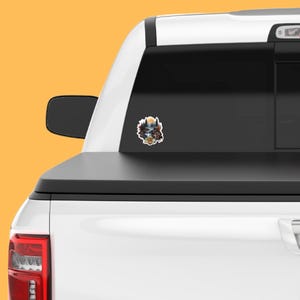 May include: A white pickup truck with a sticker on the back window. The sticker is a colorful illustration of a forest scene with a waterfall, a sun, and a bear.
