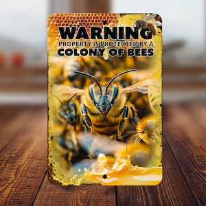 Può includere: Un cartello di avvertimento con un motivo a nido d'ape e il testo "WARNING PROPERTY IS PROTECTED BY A COLONY OF BEES". Il cartello presenta un'immagine ravvicinata di un alveare.