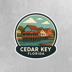 May include: A round sticker featuring a coastal scene with buildings on stilts over water. The sticker has a teal and cream border, with the text "CEDAR KEY FLORIDA" in white. The buildings have red and blue roofs, and the sky is blue with white clouds.