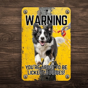 Pode incluir: Uma placa de metal retangular com fundo amarelo e a palavra "WARNING" em letras pretas grandes. Um cão preto e branco é apresentado no centro, com o texto "YOU'RE ABOUT TO BE LICKED TO PIECES!" abaixo. A placa é fixada com quatro parafusos.