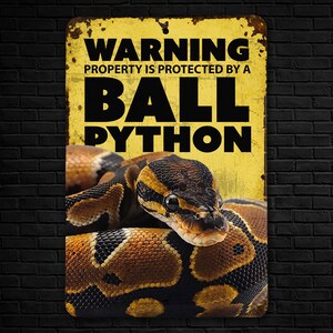 May include: A yellow warning sign with black text that reads "Warning Property is protected by a Ball Python". A ball python is curled up on the sign.