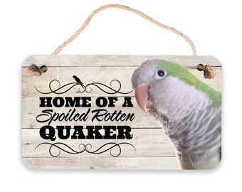 May include: A wooden sign with a whitewashed background and black text that reads "Home of a Spoiled Rotten Quaker". A green Quaker parrot is pictured on the right side of the sign.