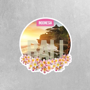 May include: A round sticker with a photo of a temple in Bali, Indonesia. The temple is on a cliff overlooking the ocean. The sticker has the word "BALI" in large white letters over the photo. The sticker is surrounded by pink flowers.