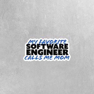 May include: A white sticker with the text "MY FAVORITE SOFTWARE ENGINEER CALLS ME MOM" in black and blue lettering. The sticker has a blue border and is set against a gray background.