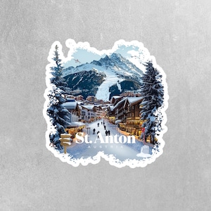 May include: A sticker featuring a snowy mountain village scene with the text "St. Anton Austria". The village is nestled in a valley with snow-covered mountains in the background. The sticker has a white border with a distressed, hand-drawn look.
