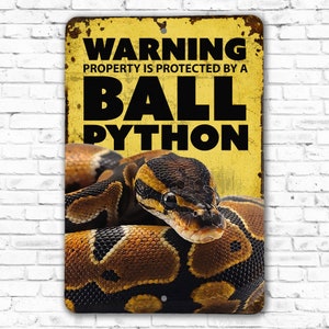 May include: Yellow warning sign with black text that reads "WARNING PROPERTY IS PROTECTED BY A BALL PYTHON". A ball python is pictured on the sign.