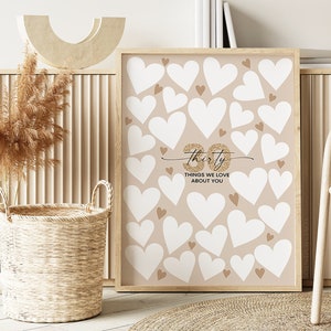 May include: A printable 30th birthday party game with a beige background and white hearts. The text "Thirty Things We Love About You" is written in gold glitter.