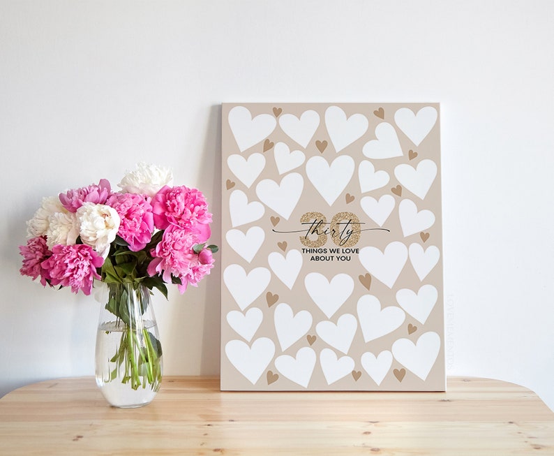 May include: A beige canvas sign with white hearts and gold glitter. The sign says "Thirty Things We Love About You".