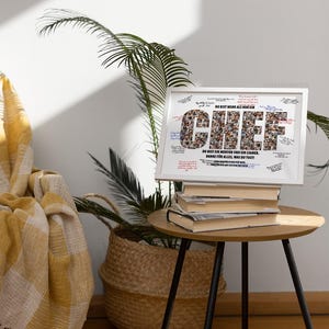 May include: A framed print with the word "CHIEF" in large letters, composed of smaller images. The frame sits atop a stack of books on a small, round table with black legs. The text "DU BIST MEHR ALS NUR EIN" is above the word "CHIEF".