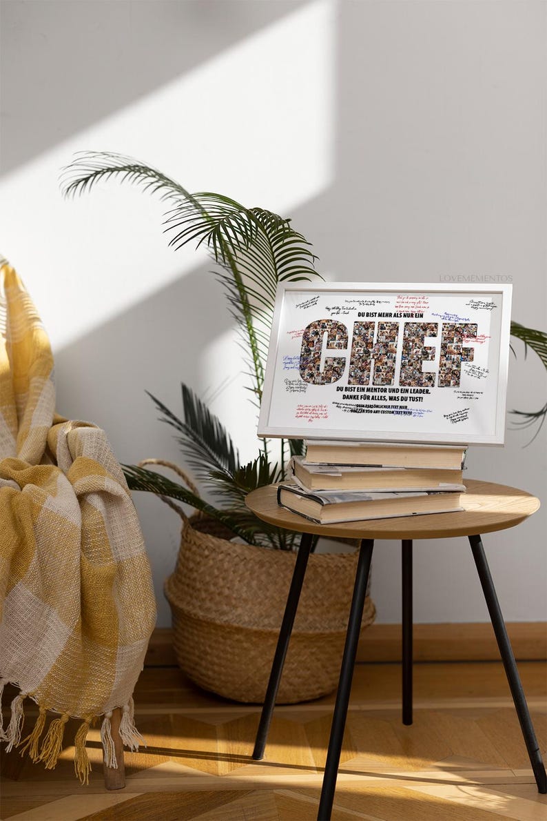 May include: A framed print with the word "CHIEF" in large letters, composed of smaller images. The frame sits atop a stack of books on a small, round table with black legs. The text "DU BIST MEHR ALS NUR EIN" is above the word "CHIEF".