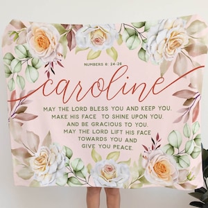 May include: A pink floral blanket with the name "Caroline" and a Bible verse from Numbers 6:24-26. The verse reads: "May the Lord bless you and keep you. Make his face to shine upon you. And be gracious to you. May the Lord lift his face towards you and give you peace."