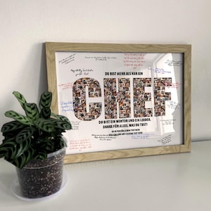May include: Framed print with the word "CHEF" in large letters, composed of smaller images. The print includes text in German, signatures, and is in a light wood frame. A potted plant is in the foreground.