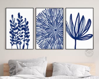 May include: A set of three framed wall art prints featuring dark blue botanical and abstract illustrations on a white background. The left print shows leafy stems, the centre shows a radial burst pattern, and the right shows a single large flower.