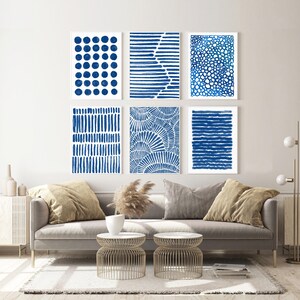 May include: A set of six abstract blue and white prints featuring different geometric patterns. The prints are arranged in a grid on a white wall above a grey sofa.