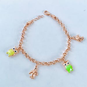 Puede incluir: Un brazalete de cadena dorada con cuatro dijes: dos búhos y dos pingüinos. Los búhos son verdes y amarillos con ojos negros. Los pingüinos son plateados.