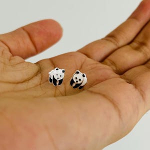 May include: A pair of silver panda bear stud earrings. The panda bears are black and white and have a shiny finish.