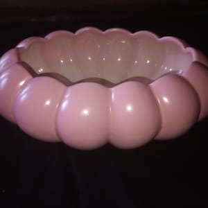 May include: A pink ceramic bowl with a scalloped rim and a rounded, bubble-like exterior. The bowl has a glossy finish and a light pink color, suitable for serving or display.
