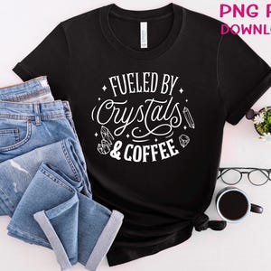 May include: Black t-shirt with white text that reads "Fueled by Crystals & Coffee". The text is surrounded by small crystal and coffee bean illustrations.