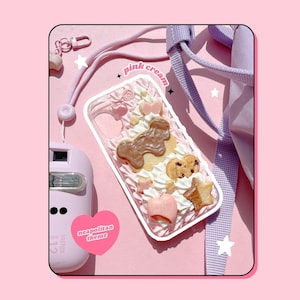 May include: A clear phone case with a Neapolitan theme, featuring a design of cookies, whipped cream, and a chocolate-covered cookie. The case is decorated with the words "pink cream". A pink camera and a pink strap are also visible.