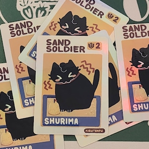 May include: Several trading cards featuring a black cat character with the text "SAND SOLDIER" and "SHURIMA". The cards have a light orange background with a blue border and a small illustration of a sand-like object.