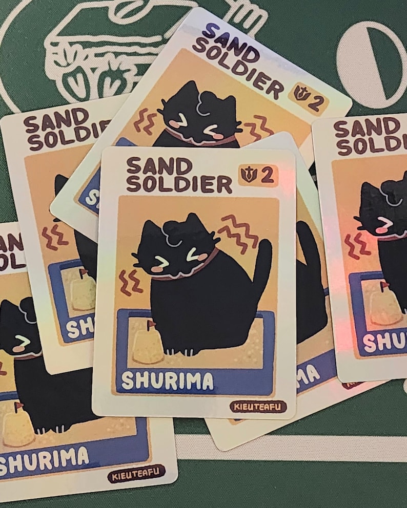 May include: Several trading cards featuring a black cat character with the text "SAND SOLDIER" and "SHURIMA". The cards have a light orange background with a blue border and a small illustration of a sand-like object.