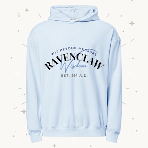 Puede incluir: Sudadera con capucha azul claro con cordón. En la parte delantera, el texto "Wit Beyond Measure Ravenclaw Wisdom" en negro y azul claro, con "Est. 991 A.D." debajo. La sudadera está hecha de un material suave.