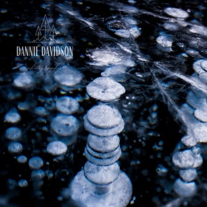 Op de afbeelding: Een close-up van een bevroren meer met een stapel ijsbellen. De bellen zijn wit en doorschijnend en zijn in een verticale stapel gerangschikt. De achtergrond is donkerblauw en de bellen worden van boven belicht.