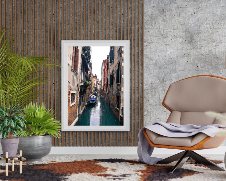 May include: A framed photograph of a narrow canal in Venice, Italy. The canal is lined with tall buildings and a small boat is visible in the water.