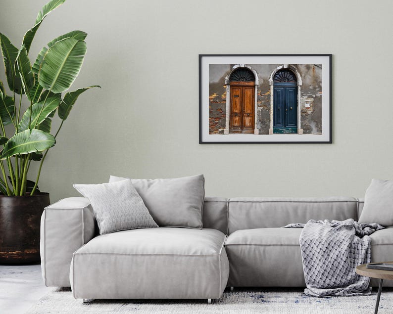 K&ouml;nnte beinhalten: Gerahmtes Foto mit zwei gew&ouml;lbten T&uuml;ren, eine braun und eine blaue, in einer verwitterten Wand. Das Bild hat einen Vintage-Look. Der Rahmen h&auml;ngt &uuml;ber einem grauen Sofa. Ein dekoratives Wandbild.