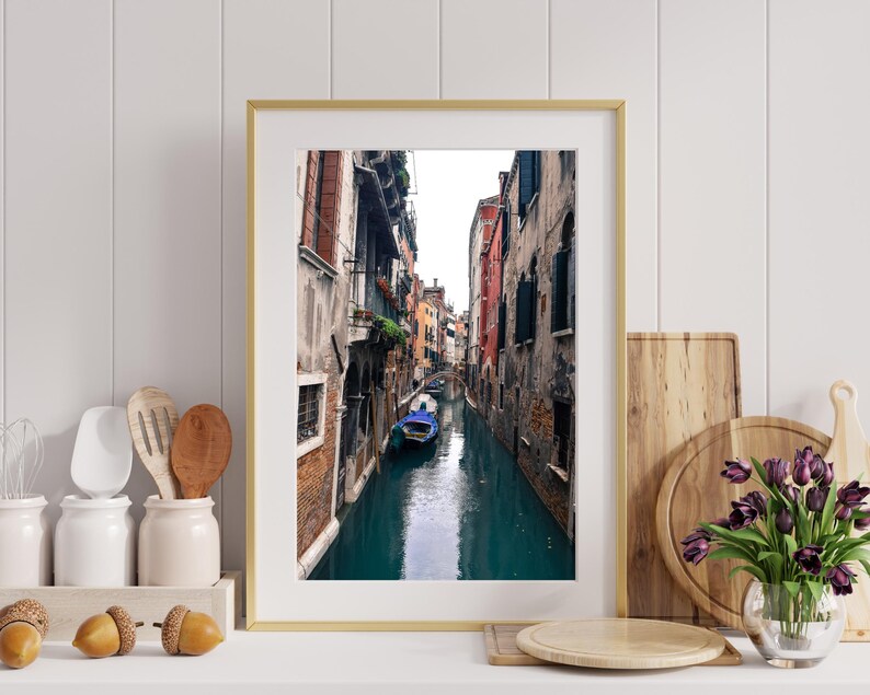 May include: A photograph of a narrow canal in Venice, Italy. The canal is lined with colorful buildings and a gondola is floating in the water.