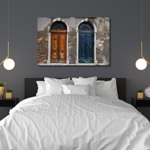 K&ouml;nnte beinhalten: Ein Schlafzimmer mit einem Leinwanddruck von zwei gew&ouml;lbten T&uuml;ren, eine braun und eine blaue, an einer verwitterten Wand. Das Bett hat eine wei&szlig;e Bettdecke, und der Raum ist mit moderner Beleuchtung und Nachttischen dekoriert.