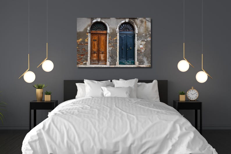 K&ouml;nnte beinhalten: Ein Schlafzimmer mit einem Leinwanddruck von zwei gew&ouml;lbten T&uuml;ren, eine braun und eine blaue, an einer verwitterten Wand. Das Bett hat eine wei&szlig;e Bettdecke, und der Raum ist mit moderner Beleuchtung und Nachttischen dekoriert.