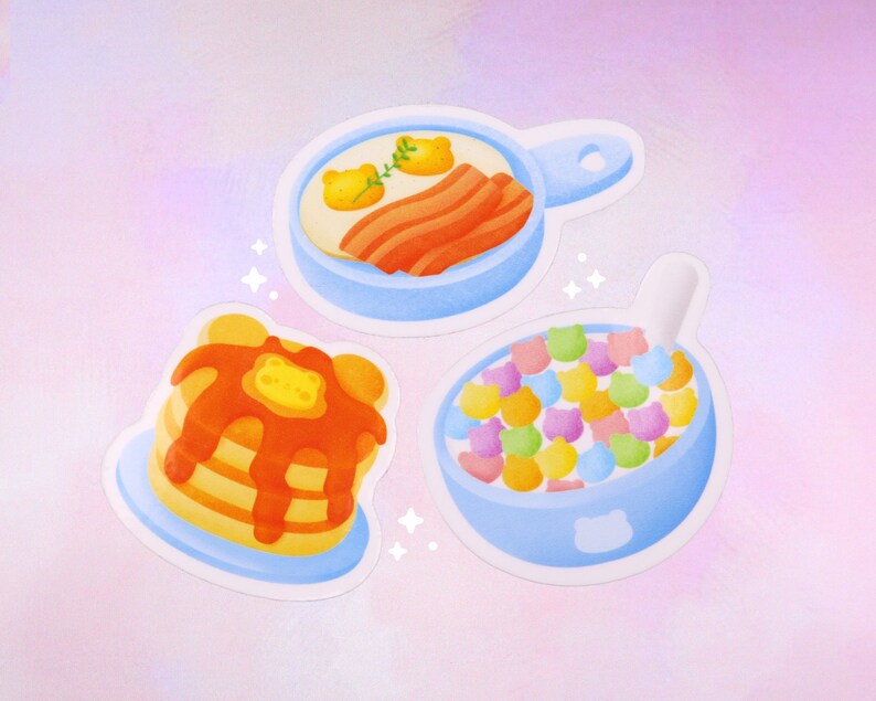 Puede incluir: Tres pegatinas azules y blancas con ilustraciones de alimentos para el desayuno. La primera pegatina muestra una sart&eacute;n azul con un huevo frito, tocino y una ramita de perejil. La segunda pegatina muestra una pila de panqueques con jarabe y una porci&oacute;n de mantequilla. La tercera pegatina muestra un taz&oacute;n azul lleno de cereal colorido y una cuchara.