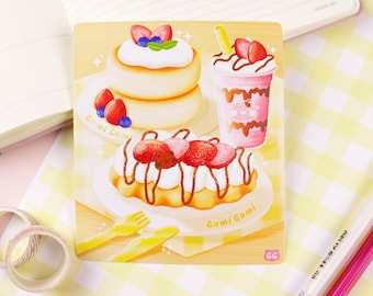 May include: A colorful illustration of three desserts: a stack of fluffy pancakes with whipped cream and strawberries, a waffle with chocolate sauce and strawberries, and a pink milkshake with chocolate drizzle and a straw. The text "Gomi Gomi" appears twice on the image.