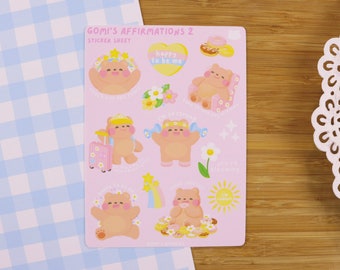 May include: A pink sticker sheet titled "Gomi's Affirmations 2" featuring cartoon bears with floral accents and positive affirmations. The sheet includes images of bears with a suitcase, dumbbells, and a heart-shaped design.