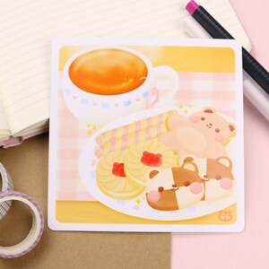 May include: A yellow and pink illustration of a cup of tea, a plate of cookies, and two bear-shaped cookies. The cookies are decorated with pink and brown frosting. The plate is on a pink and white checkered tablecloth.
