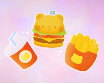 May include: Three cartoon bear-shaped stickers: a burger, fries, and a soda. The burger is yellow with a green lettuce, red tomato, and yellow cheese. The fries are yellow and in a red container. The soda is red with a yellow straw.