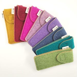 Può includere: Una collezione di custodie in feltro colorate in varie tonalità, tra cui giallo, rosso, rosa, viola, blu, verde acqua e verde. Ogni custodia ha una chiusura a patta e una piccola etichetta bianca. Le custodie sono disposte a semicerchio.