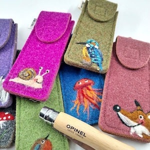 Könnte beinhalten: Eine Auswahl an farbigen Filz-Messertaschen, jede mit einem einzigartigen Tier- oder Naturmotiv verziert. Ein Opinel-Messer mit Holzgriff ist teilweise sichtbar. Designs umfassen eine Schnecke, einen Vogel, einen Fuchs und eine Qualle.