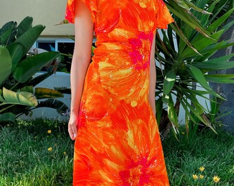 May include: A long orange and yellow floral print dress with short sleeves and a scoop neck. The dress is made of a lightweight fabric and has a flowy silhouette.