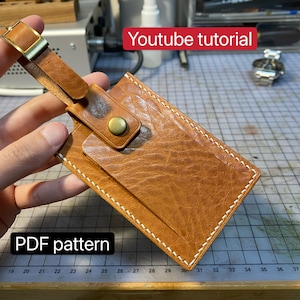 Peut inclure: Une étiquette à bagages en cuir marron avec une bordure cousue blanche et une boucle en laiton. L'étiquette a une petite poche pour une carte ou une pièce d'identité. Le texte "PDF pattern" et "Youtube tutorial" est visible sur l'image.