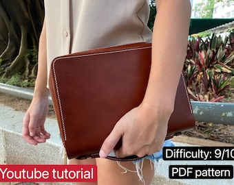 May include: A brown leather clutch with white stitching. The clutch is being held by a person wearing a light beige shirt and blue denim shorts. The text "Difficulty: 9/10" and "PDF pattern" is visible in the image.