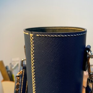 May include: A dark blue cylindrical leather bag with a cream-colored stitched seam and a silver chain strap.