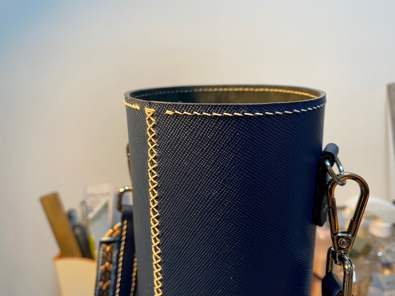 May include: A dark blue cylindrical leather bag with a cream-colored stitched seam and a silver chain strap.